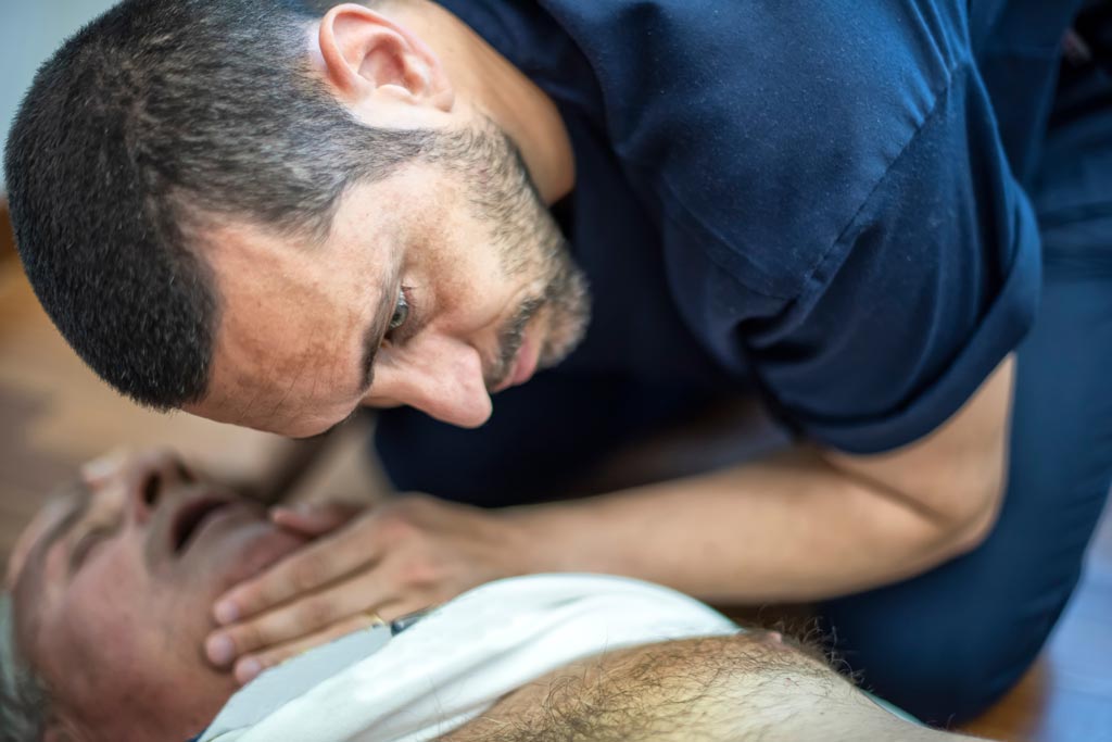Man checks for breathing in unconscious elderly man experiencing cardiac arrest.